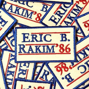 May include: Cream-colored embroidered patches with the text "ERIC B. RAKIM '86" in blue and red. The patches have a rectangular shape with a blue border. The text is centered on the patch.