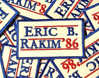 May include: Cream-coloured embroidered patches featuring the text "ERIC B. RAKIM '86" in blue and red. The patches are rectangular with a blue border. The text is centrally positioned on the patch.