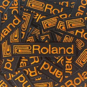 Könnte beinhalten: Eine Sammlung rechteckiger, schwarz bestickter Aufnäher mit dem orangefarbenen Roland-Logo und Schriftzug. Jeder Aufnäher zeigt ein stilisiertes orangefarbenes Grafiksymbol auf der linken Seite, gefolgt vom Wort Roland in orangefarbenem Garn.