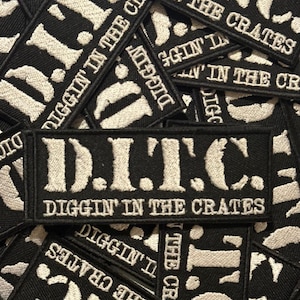 Pode incluir: Patch retangular preto com texto bordado branco. O patch diz "D.I.T.C." acima de "DIGGIN' IN THE CRATES". Vários patches são visíveis, sobrepostos. Os patches são provavelmente para roupas ou acessórios.