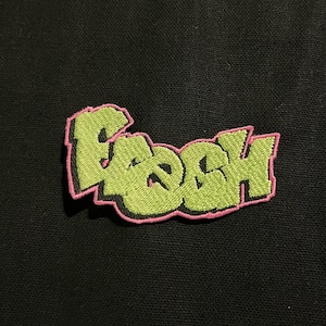 Puede incluir: Parche bordado con la palabra "Fresh" en letras verdes con contorno rosa. El parche está sobre un fondo negro. Adecuado para ropa o accesorios.