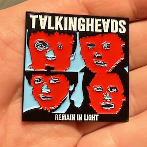 Puede incluir: Pin cuadrado de esmalte con la portada del álbum de Talking Heads. El pin tiene un borde negro con el nombre de la banda en letras blancas en la parte superior. Cuatro caras rojas están en el centro, con las palabras "Remain in Light" en la parte inferior.
