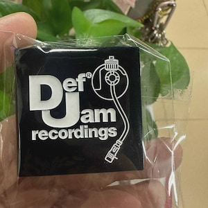 May include: Black square sticker with the text "Def Jam recordings" in white. The sticker features a graphic of a record player needle and plug. The sticker is in a clear plastic wrapper.