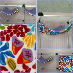 Puede incluir: Varios peque&ntilde;os columpios para mascotas colgando en una jaula. Los columpios est&aacute;n hechos de tela suave de color lavanda con un colorido estampado floral en los bordes. El estampado floral incluye flores rojas, naranjas, azules y amarillas. La jaula es blanca.