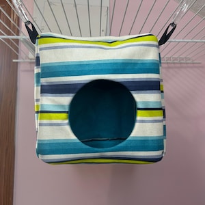 Puede incluir: Una cama colgante de tela a rayas para mascotas pequeñas, con un esquema de color azul, blanco y amarillo. La cama tiene una abertura redonda para la entrada.