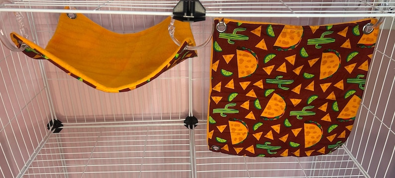 Puede incluir: Una peque&ntilde;a jaula para mascotas con dos accesorios colgantes. Uno es una hamaca amarilla con un ribete estampado. El otro es una tela marr&oacute;n con un estampado de tacos, gajos de lima y cactus. Ambos est&aacute;n dise&ntilde;ados para mascotas peque&ntilde;as.