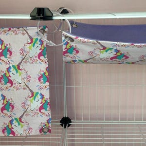 Puede incluir: Dos accesorios para mascotas: un panel de tela rectangular y una hamaca. Ambos est&aacute;n decorados con un patr&oacute;n repetido de unicornios con crines coloridas y detalles florales sobre un fondo rosa claro. La hamaca tiene un interior morado.