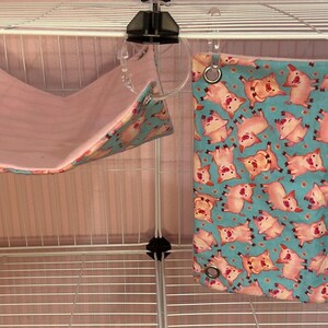 Puede incluir: Dos accesorios para mascotas: una hamaca rosa y una cama cuadrada turquesa. La hamaca est&aacute; suspendida de la jaula con clips de pl&aacute;stico transparente. La cama cuadrada presenta un estampado de cerdos rosas sobre fondo turquesa, con ojales met&aacute;licos.