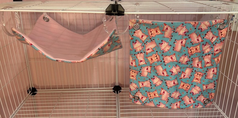 Puede incluir: Dos accesorios para mascotas: una hamaca rosa y una cama cuadrada turquesa. La hamaca est&aacute; suspendida de la jaula con clips de pl&aacute;stico transparente. La cama cuadrada presenta un estampado de cerdos rosas sobre fondo turquesa, con ojales met&aacute;licos.