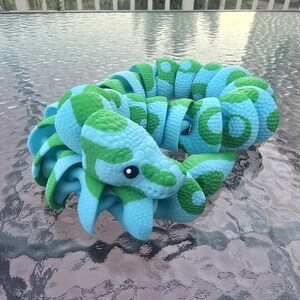 May include: A blue and green toy snake with a segmented body and a detailed head. The snake has a pattern of green spots and stripes on a blue background. The toy is made of a flexible material and is designed to be bendable.