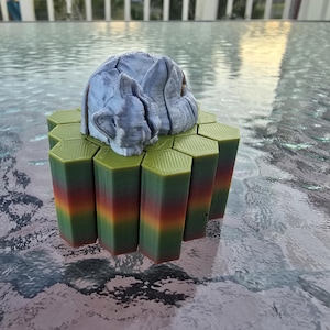 May include: A 3D-printed sculpture of a sleeping rabbit rests atop a hexagonal platform. The platform's columns transition from green to orange and red. The rabbit is a light gray color, and the platform is made of plastic.