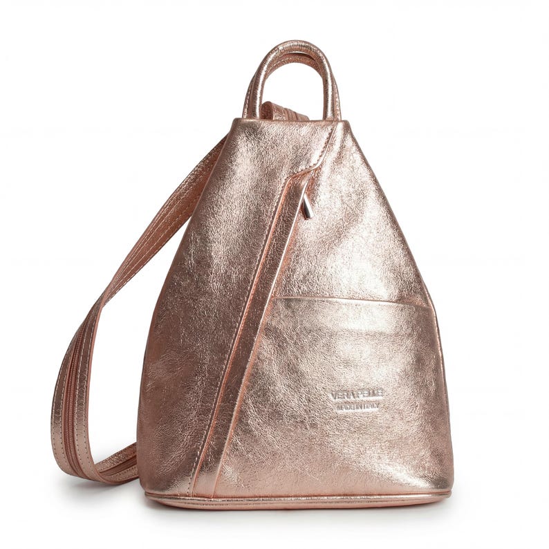 May include: A rose gold backpack with a metallic finish. The bag has a top handle, adjustable straps, and a front pocket. A diagonal zipper runs down the front. The bag is made of a shiny, textured material.