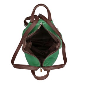 May include: Open green backpack with brown straps and handles. The bag has a zippered main compartment and a brown interior lining. The straps are adjustable, and the bag appears to be made of a smooth material.