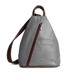 May include: Gray leather backpack with brown accents. Features a top handle and adjustable shoulder straps. The backpack has a front pocket and a diagonal brown stripe. The text "VERA PELLE MADE IN ITALY" is visible on the front.
