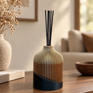 Peut inclure: Un diffuseur à roseaux doté d'une base cylindrique à lattes verticales avec un dégradé de couleurs passant du crème en haut au brun clair au milieu et au noir uni à la base, avec plusieurs tiges noires fines insérées dedans.