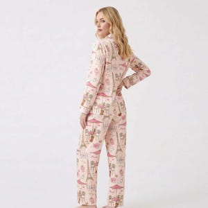 May include: A light pink pajama set with a repeating pattern of Parisian cafe scenes, including the Eiffel Tower, cafe tables, and pastries. The long-sleeved top and trousers are made of a soft material.