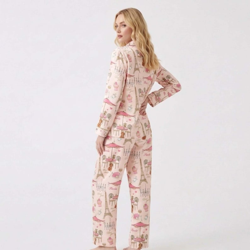 May include: A light pink pajama set with a repeating pattern of Parisian cafe scenes, including the Eiffel Tower, cafe tables, and pastries. The long-sleeved top and trousers are made of a soft material.