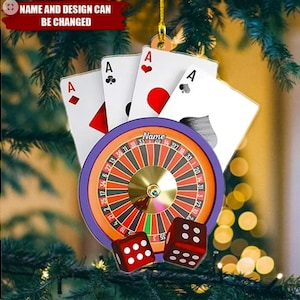May include: Casino-themed Christmas ornament featuring a roulette wheel, dice, and playing cards. The ornament includes four Ace playing cards and two red dice. The roulette wheel has a purple border and a gold center. The text "Name and Design Can Be Changed" is at the top.
