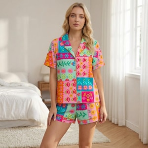 May include: A colorful pajama set featuring a patchwork design with floral and geometric patterns in pink, teal, orange, and green. The set includes a short-sleeved button-down shirt and matching shorts. The outfit is made of a lightweight fabric.