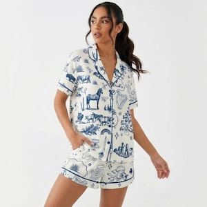 Puede incluir: Conjunto de pijama blanco con un dise&ntilde;o azul ilustrado con caballos, arpas y otros motivos. La parte superior de manga corta y los pantalones cortos tienen ribetes azules. El conjunto est&aacute; hecho de tela ligera.