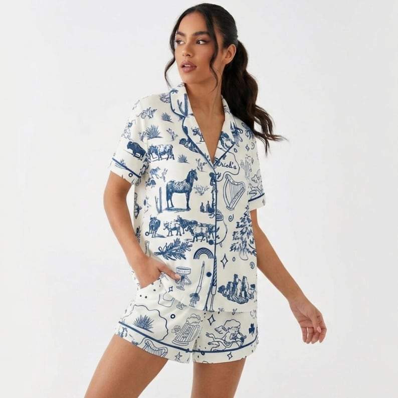 Puede incluir: Conjunto de pijama blanco con un dise&ntilde;o azul ilustrado con caballos, arpas y otros motivos. La parte superior de manga corta y los pantalones cortos tienen ribetes azules. El conjunto est&aacute; hecho de tela ligera.