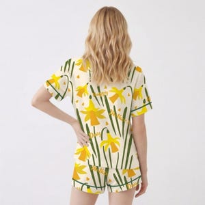 May include: Cream-colored pajama set with a yellow daffodil pattern and the text "Happy Mother's Day". The set includes a short-sleeved top and matching shorts. The design features yellow flowers, green stems, and leaves.