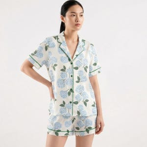 May include: White pajama set with a blue floral pattern. The short-sleeved top and shorts are trimmed with green piping. The set features a button-down shirt and shorts, perfect for a comfortable night's sleep.