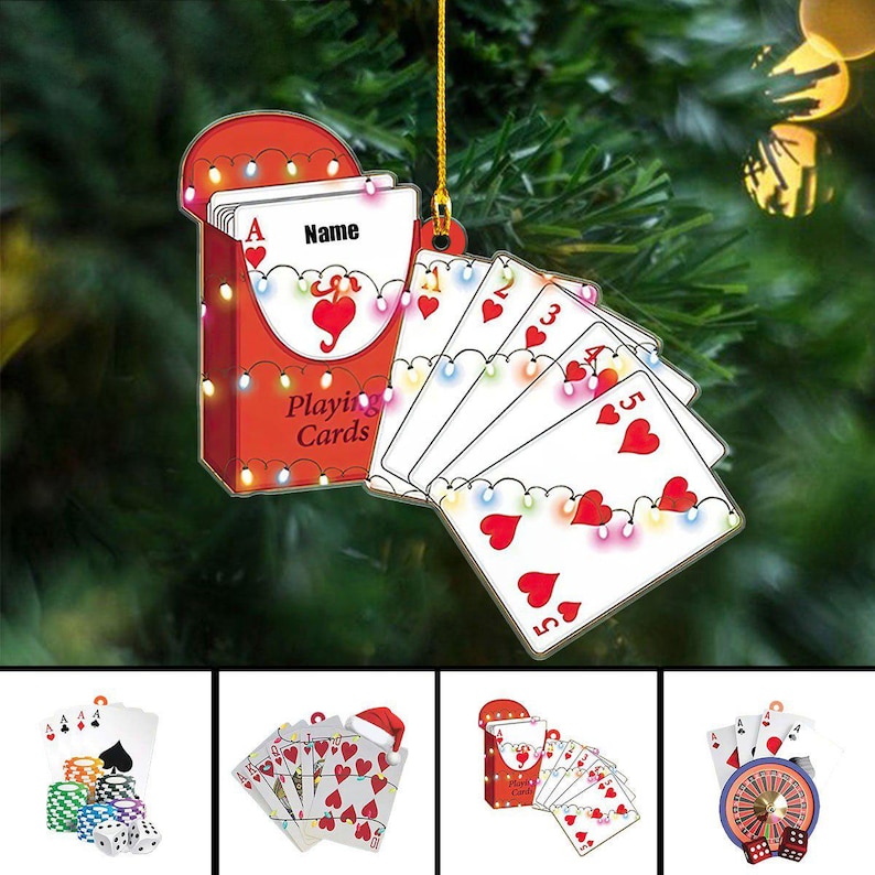 May include: A red and white playing card ornament with a deck of cards and a fan of cards. The deck of cards has the word "Name" on it. The cards are decorated with hearts and lights. The words "Playing Cards" are on the box.