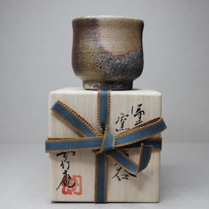以下が含まれることがあります： ざらざらとした質感の小さな茶色と灰色の陶器のカップが、青と茶色のリボンで結ばれた木製の箱の上に置かれています。箱には日本語が書かれています。