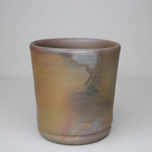 May include: A ceramic cup with a brown, yellow, and grey glaze. The cup has a rounded shape and a slightly flared rim.