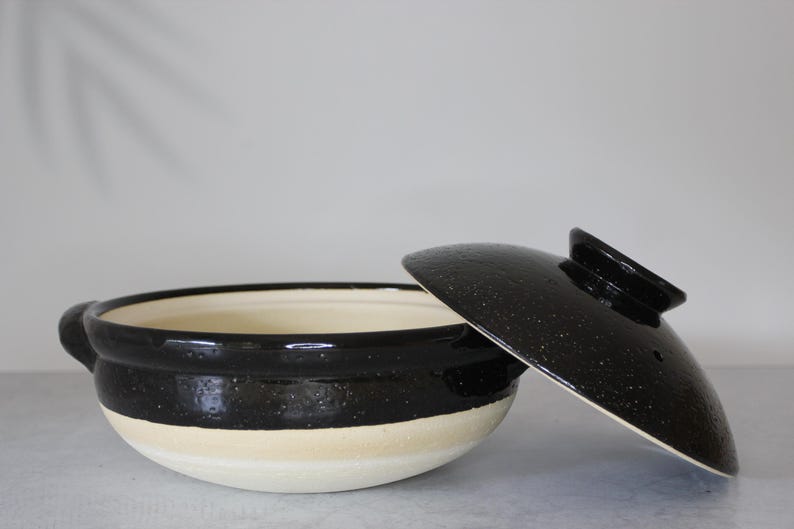 Peut inclure: Un pot de cuisson en c&eacute;ramique noir et cr&egrave;me avec un couvercle assorti. Le pot a une forme arrondie avec un bord noir et une base cr&egrave;me. Le couvercle est noir avec une finition mouchet&eacute;e. Le pot a deux petites poign&eacute;es.