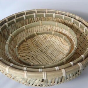 May include: A set of three round, nested baskets crafted from natural light-colored bamboo strips. Each basket features a reinforced circular rim with light-colored binding and a woven base, showcasing a consistent, open-weave pattern throughout.