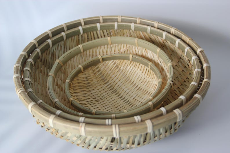 May include: A set of three round, nested baskets crafted from natural light-colored bamboo strips. Each basket features a reinforced circular rim with light-colored binding and a woven base, showcasing a consistent, open-weave pattern throughout.