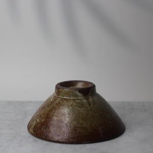 Puede incluir: Un cuenco de cer&aacute;mica hecho a mano con una forma c&oacute;nica invertida inusual. El cuenco presenta un borde marr&oacute;n oscuro y un degradado de tonos terrosos, incluyendo marr&oacute;n y verde oliva. El cuenco probablemente se utiliza para servir o exhibir.