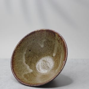 Puede incluir: Un cuenco de cer&aacute;mica hecho a mano con una forma org&aacute;nica. El cuenco presenta un interior moteado de color verde oliva y un borde marr&oacute;n oscuro. El exterior tiene un aspecto texturizado y terroso. Ideal para servir o como pieza decorativa. Medidas en cent&iacute;metros.