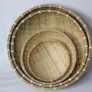 May include: A set of three round, nested baskets crafted from light-colored woven bamboo strips. Each basket features a sturdy, reinforced circular rim secured with thin, light-colored binding material, creating a consistent, layered, and circular design.
