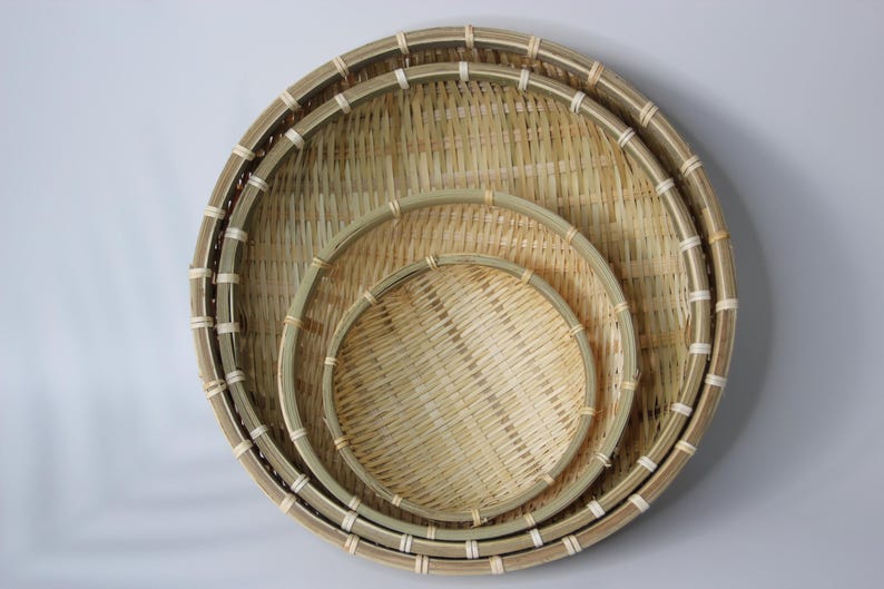 May include: A set of three round, nested baskets crafted from light-colored woven bamboo strips. Each basket features a sturdy, reinforced circular rim secured with thin, light-colored binding material, creating a consistent, layered, and circular design.