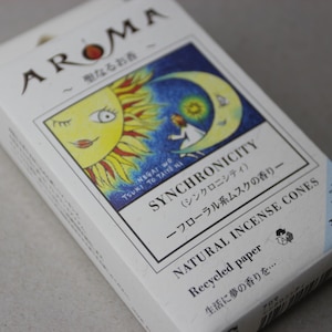 May include: A white box of natural incense cones. The box features the word "AROMA" and a colorful illustration of a sun and moon. The text on the box reads "SYNCHRONICITY" and "NATURAL INCENSE CONES".