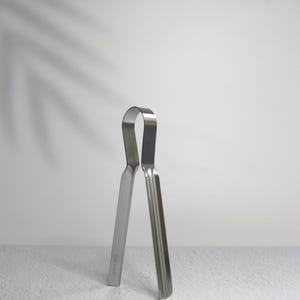以下が含まれることがあります： 滑らかで光沢のある仕上げの銀色の金属製トング。トングはU字型のハンドルが2本のまっすぐな平らなアームを繋いでいます。金属は反射する表面を持ち、デザインはシンプルで機能的です。
