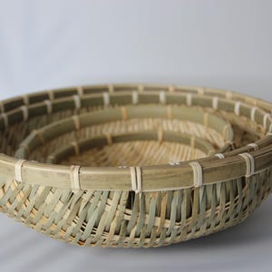 May include: A set of three nested round baskets crafted from natural bamboo strips. Each basket features a woven base and sides with a reinforced rim secured by light-colored binding. The bamboo displays varying shades of green and tan.