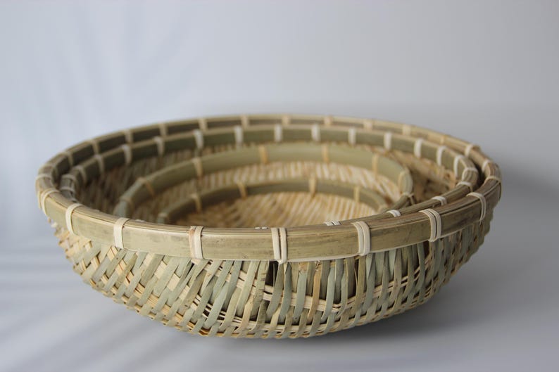 May include: A set of three nested round baskets crafted from natural bamboo strips. Each basket features a woven base and sides with a reinforced rim secured by light-colored binding. The bamboo displays varying shades of green and tan.