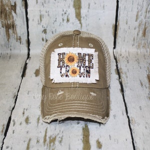 May include: A brown and beige distressed trucker hat with a patch that says "Home Grown" with sunflowers.