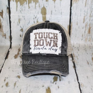 May include: A black and brown distressed trucker hat with a white patch that says "Touch Down kinda day".