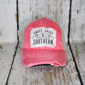 May include: A pink and brown distressed trucker hat with a white patch that says "Sweet, Sassy & Southern".