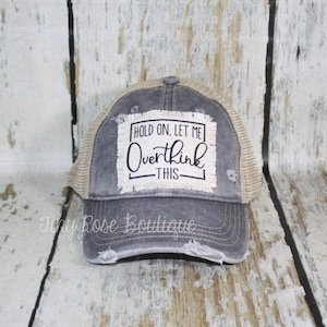 May include: A gray and beige distressed trucker hat with a white patch that says "Hold on, let me overthink this".
