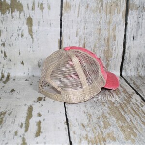 Pu&ograve; includere: Un cappello da camionista in rete rosa e beige con un aspetto usurato. Il cappello ha una visiera curva e una parte posteriore in rete.