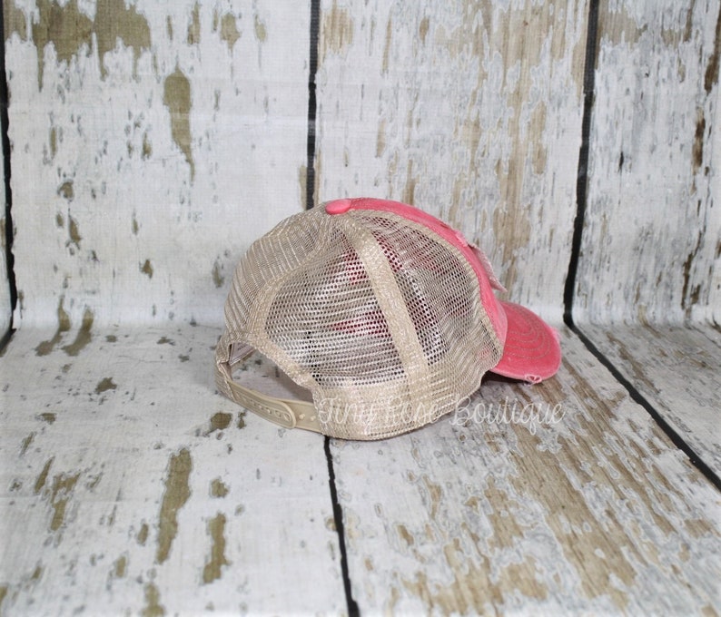 Pu&ograve; includere: Un cappello da camionista in rete rosa e beige con un aspetto usurato. Il cappello ha una visiera curva e una parte posteriore in rete.
