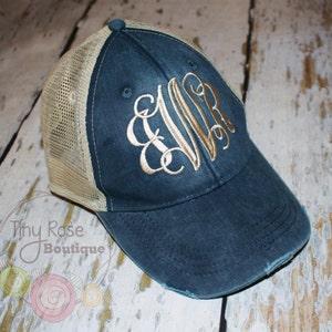 May include: A blue and beige distressed trucker hat with a gold embroidered monogram "EWR".