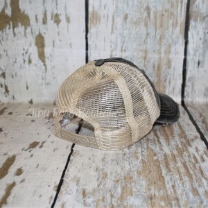 Pu&ograve; includere: Un cappello da baseball in rete nero e beige con un aspetto usurato. Il cappello ha una visiera nera e una rete beige sul retro.