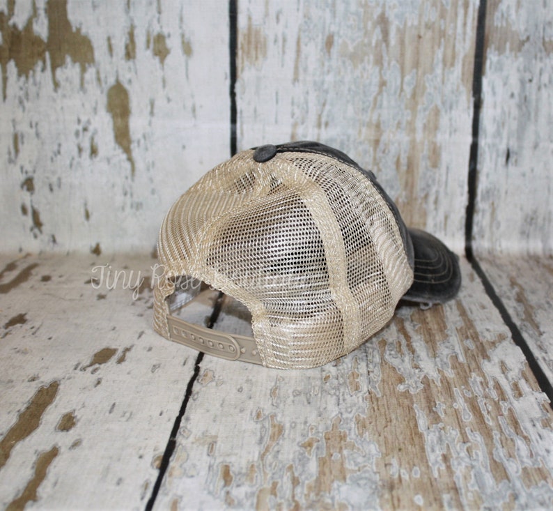 Pu&ograve; includere: Un cappello da baseball in rete nero e beige con un aspetto usurato. Il cappello ha una visiera nera e una rete beige sul retro.